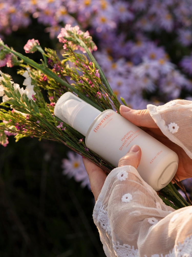 Crème hydratante vergetures Flowerchild tenue dans les mains avec un bouquet de fleurs sauvages, soin naturel pour la maternité.